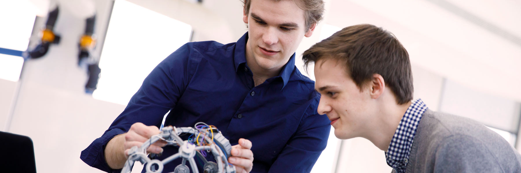 Two students examine a robotic device. 